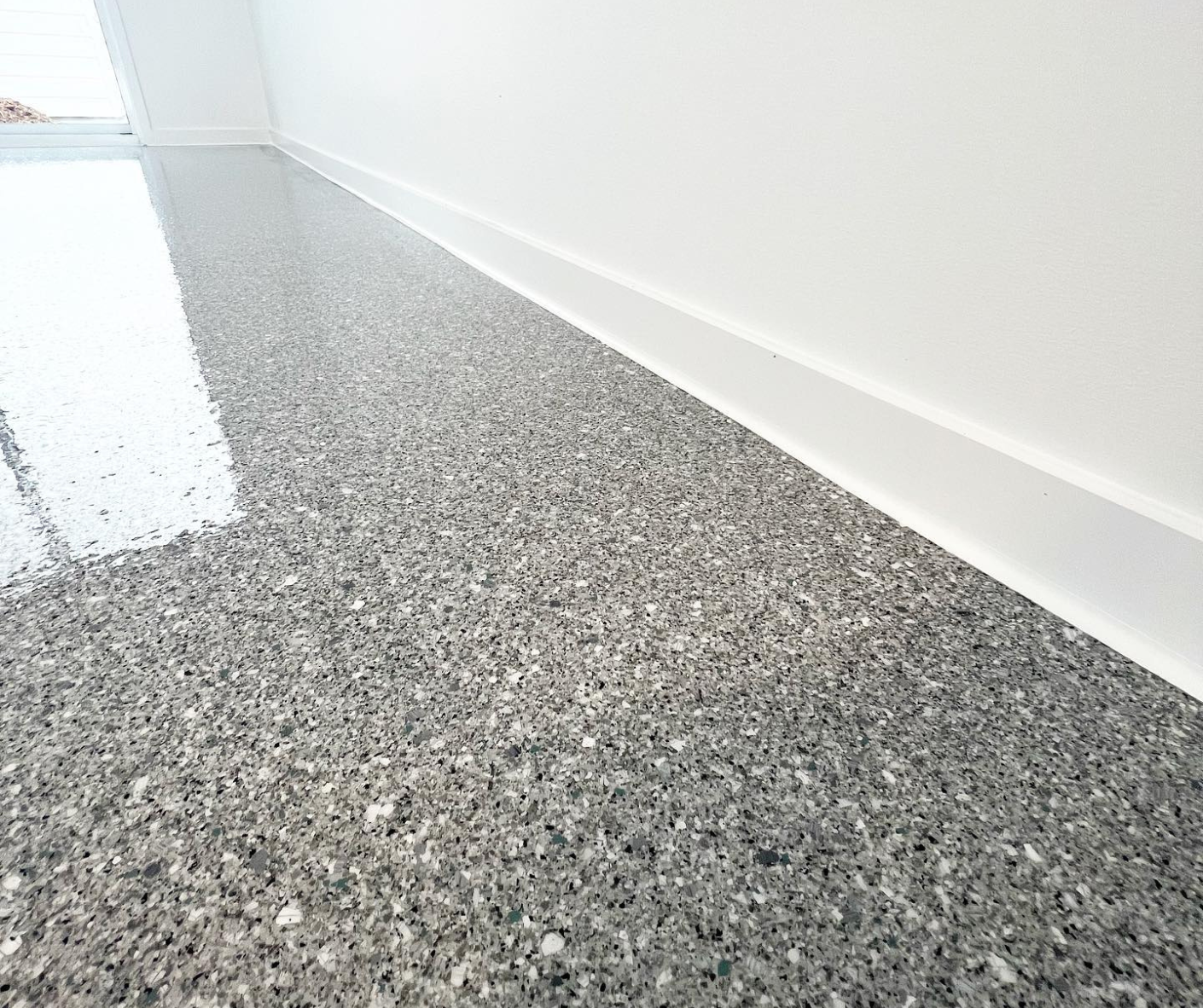Gray speckled epoxy floor meeting a white wall in a bright, empty room Gray speckled epoxy floor meeting a white wall in a bright, empty room