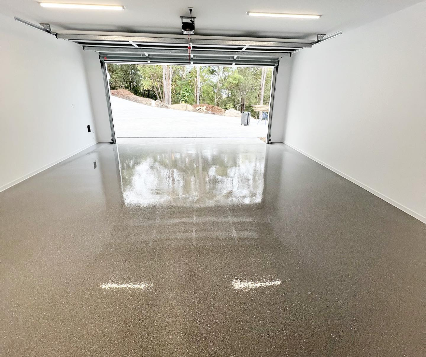 Empty garage with polished concrete floor and open door to a driveway outside Empty garage with polished concrete floor and open door to a driveway outside