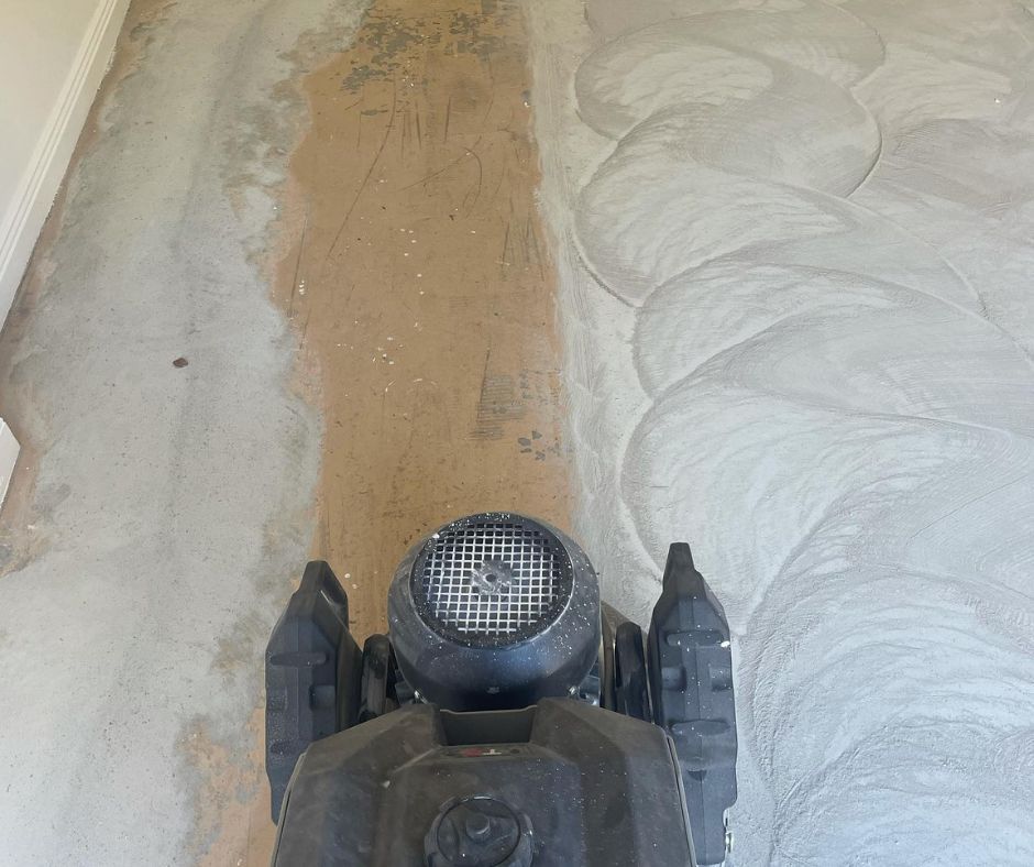 A floor sander machine moves across a concrete surface, preparing it for sealing.