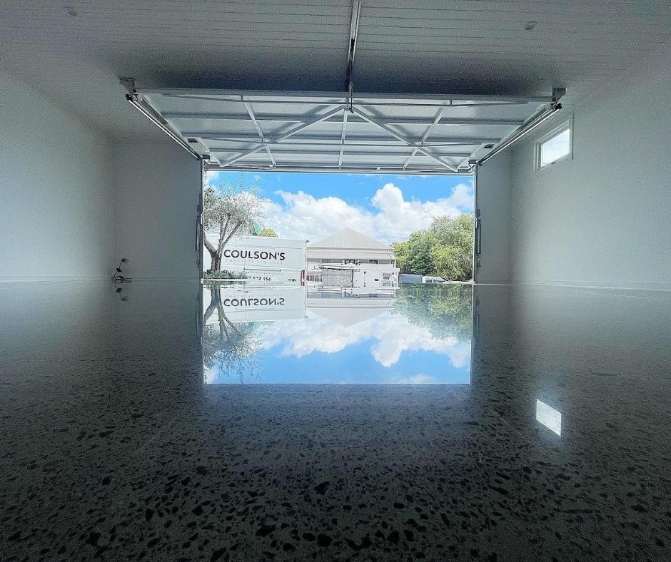 A polished concrete floor reflects the bright blue sky seen through an open garage door.
