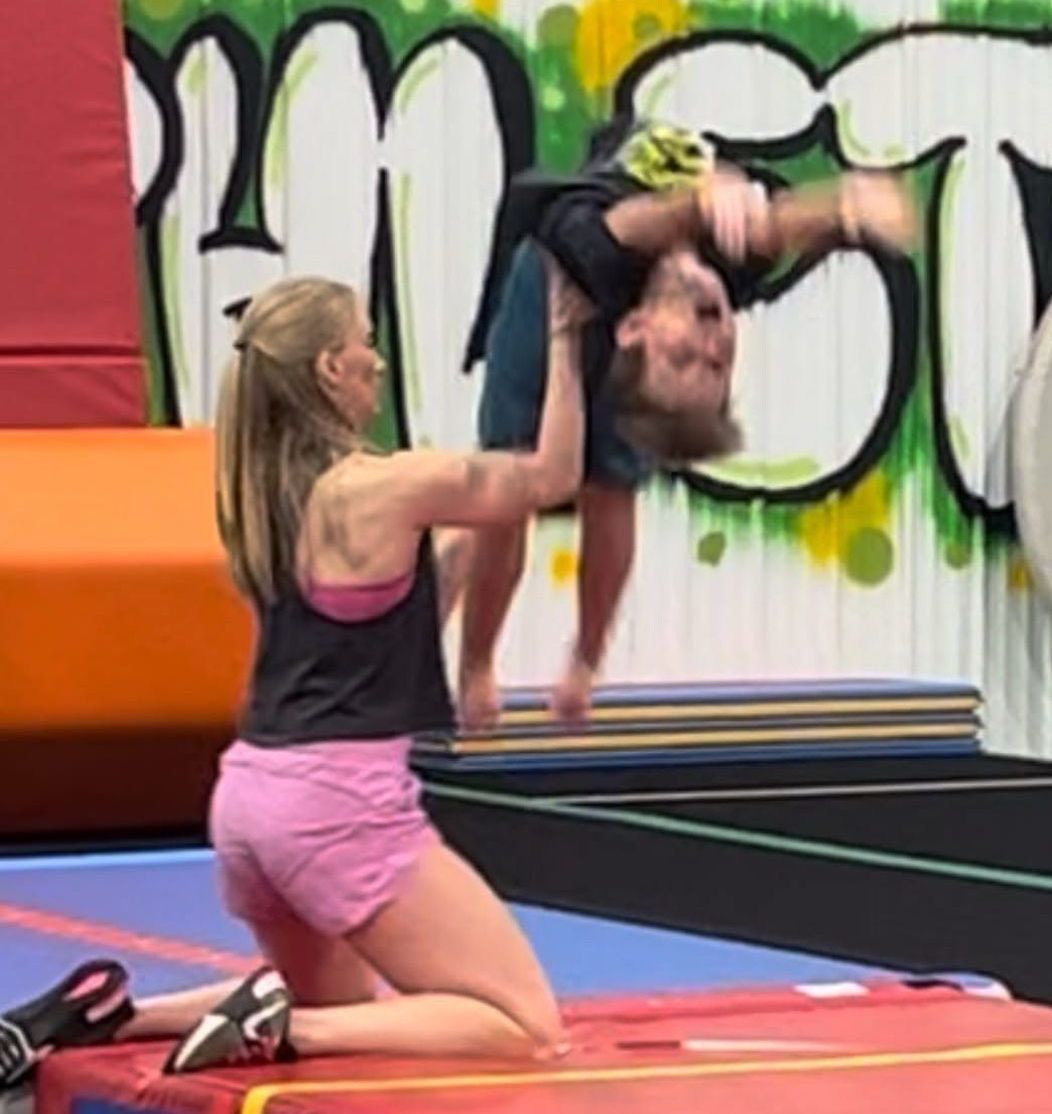 A woman is helping a man do a handstand on a mat.