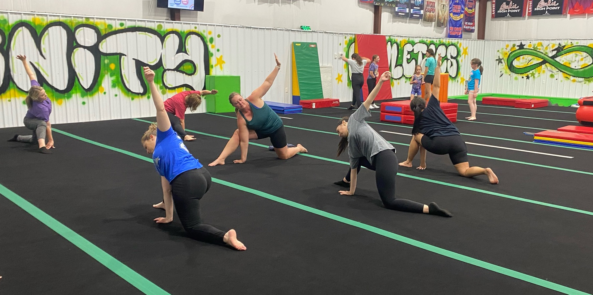 A group of people are doing stretching exercises on a gym floor.