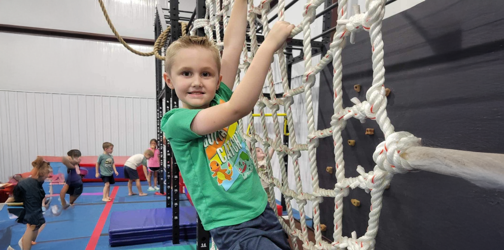 A young boy is climbing a rope ladder in a gym.