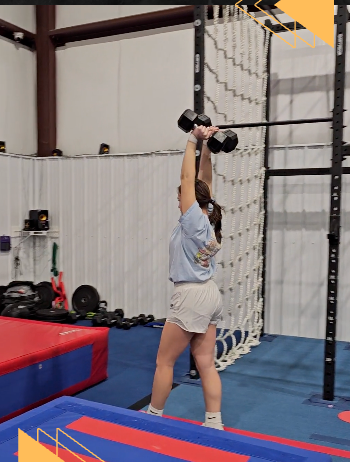 A woman is lifting a dumbbell over her head in a gym.