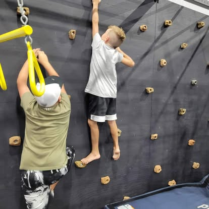 A man and a boy are climbing a climbing wall.