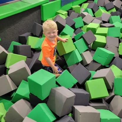 A young boy is sitting in a pile of green and gray foam cubes.
