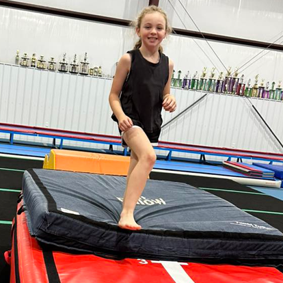 A young girl is standing on a mat in a gym.