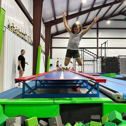 A young girl is jumping on a trampoline in a gym.