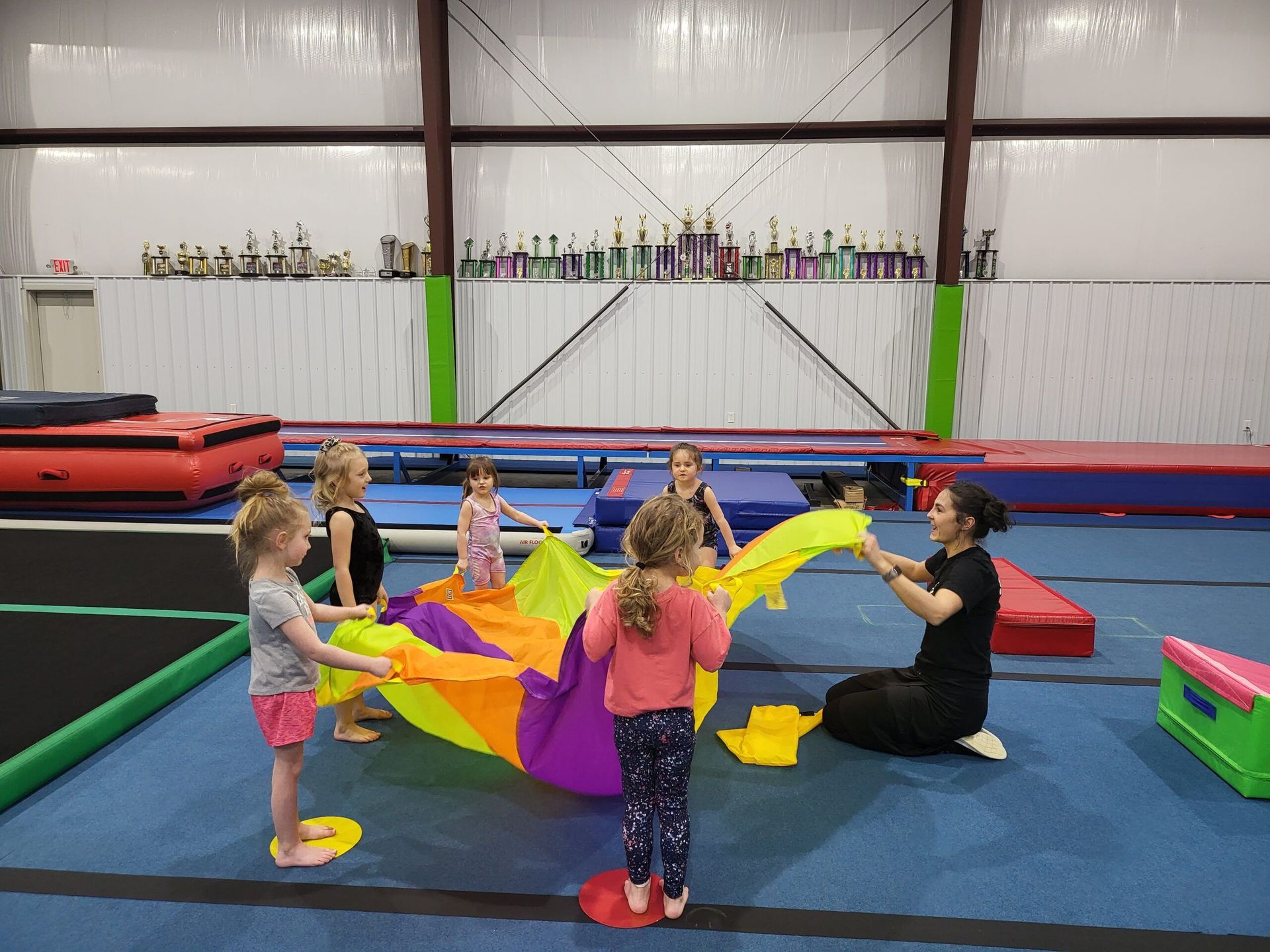 A group of young girls are playing with a parachute in a gym.