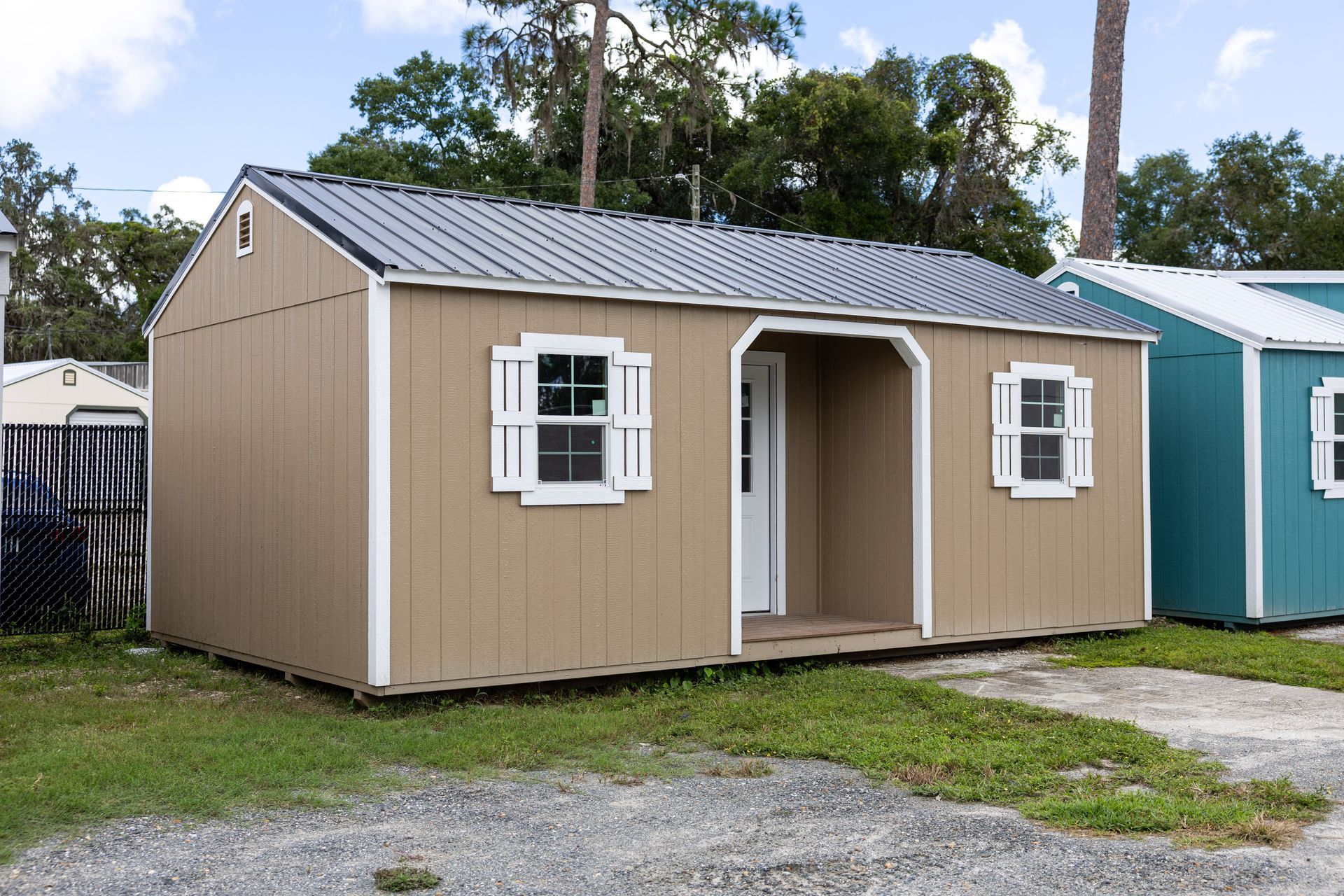 Tan shed with white trim, black roof, and two windows. Outdoors, on grass.