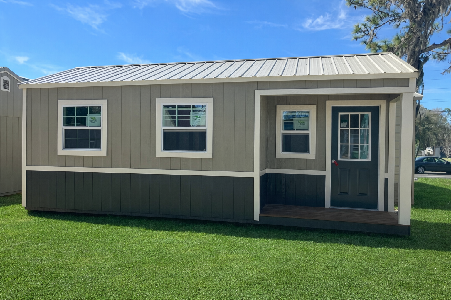 Row of colorful cabins with porches, nestled near a wooded area with green grass and a gravel path.