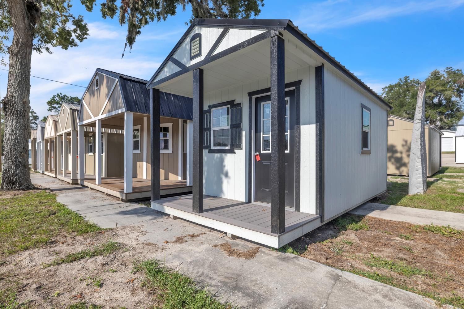 Row of colorful cabins with porches, nestled near a wooded area with green grass and a gravel path. Row of colorful cabins with porches, nestled near a wooded area with green grass and a gravel path.