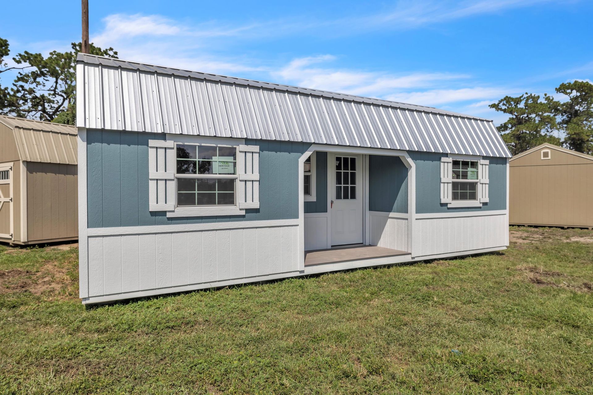 Blue and white storage shed with a metal roof on green grass.