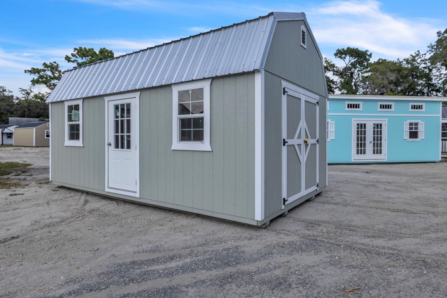 Light green shed with barn-style roof, white trim and metal roof, gray gravel ground. Blue building in background.