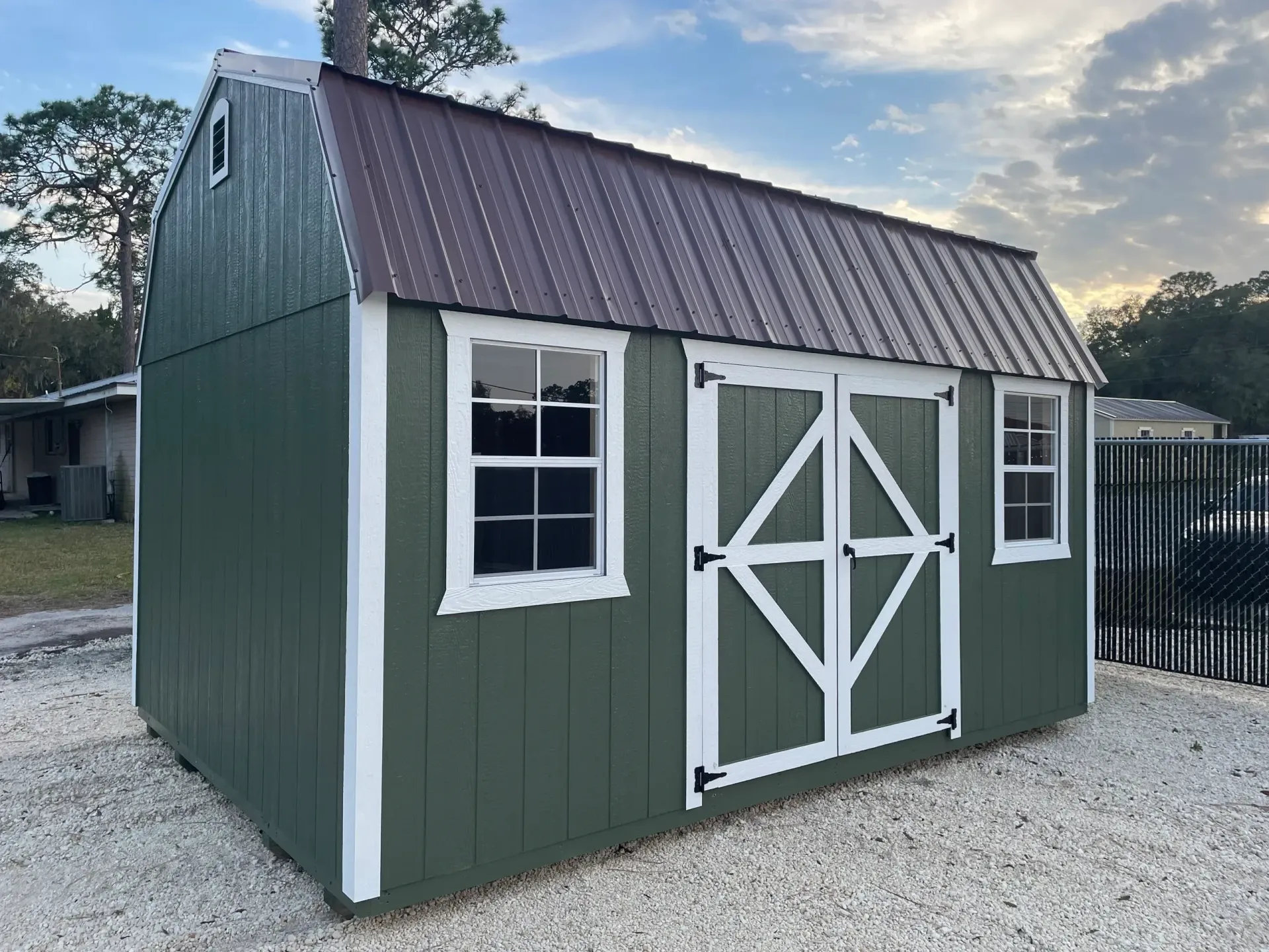 Green shed with white trim, brown metal roof, two windows, and double doors.