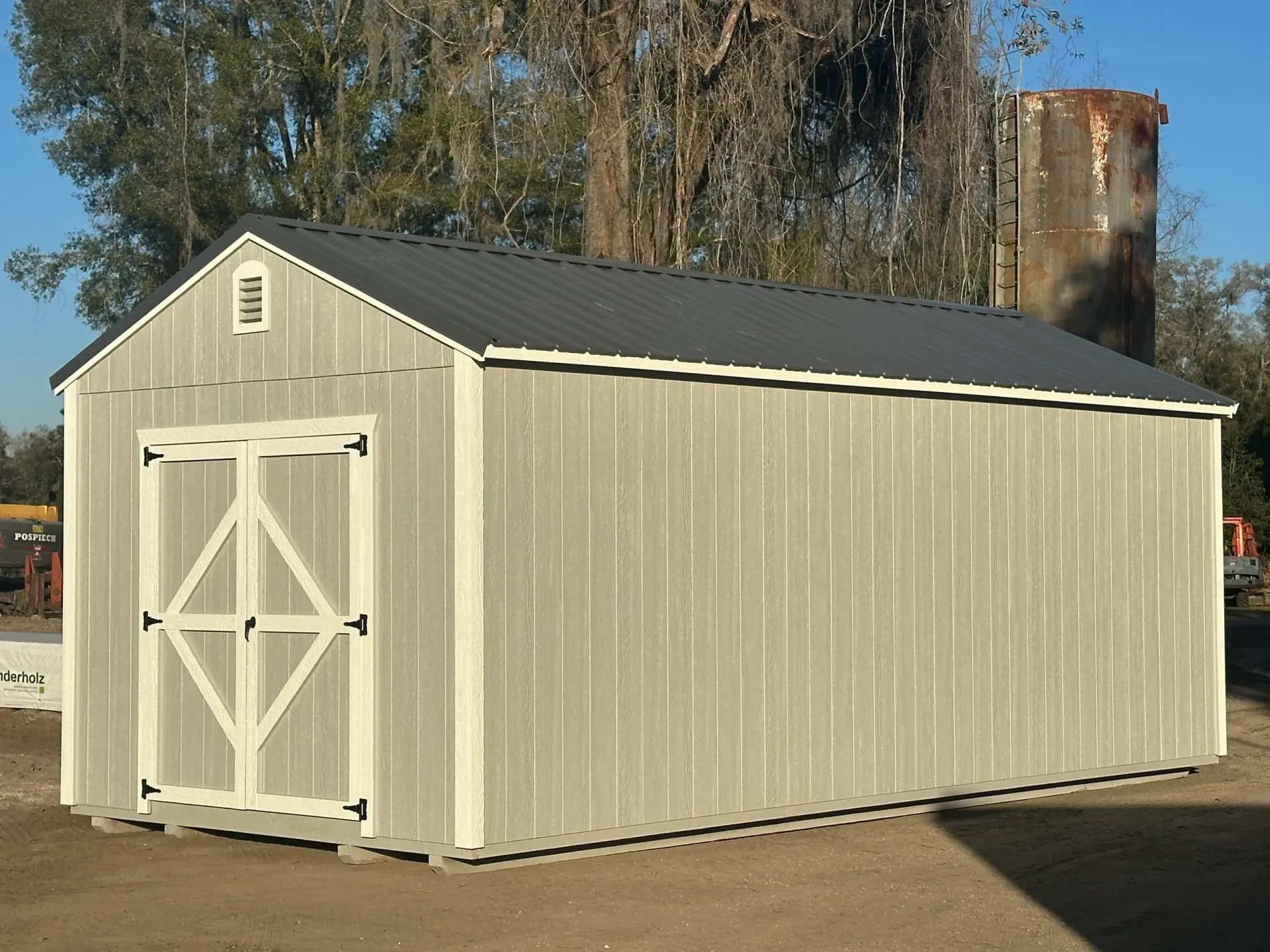 Gray shed with a dark roof and white-trimmed double doors.