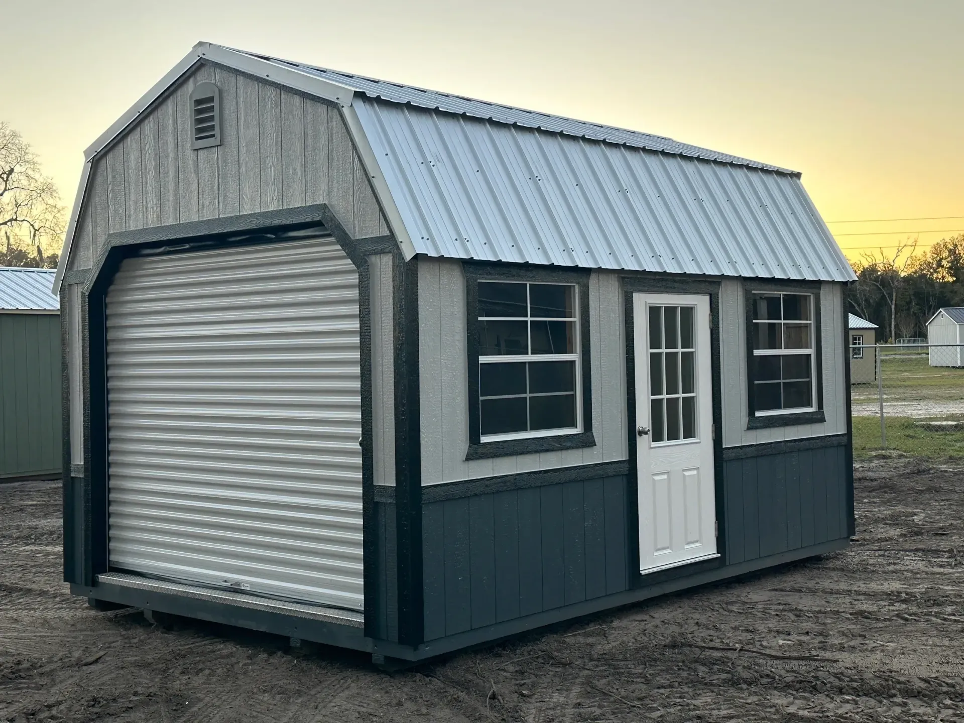 Gray and blue storage shed with roll-up door, windows, and white door; metal roof.