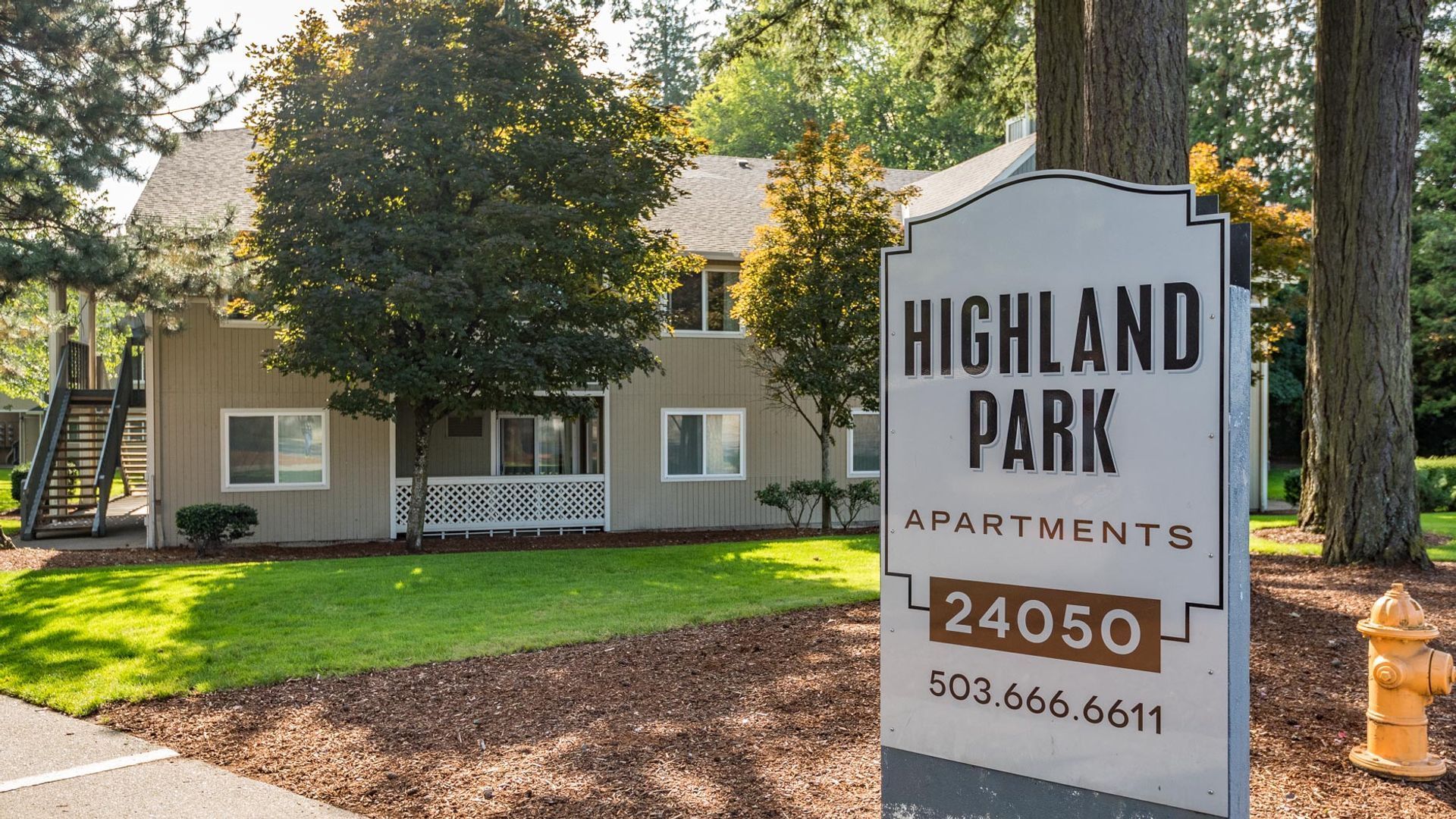 A sign for Highland Park Apartments at 24050 with a phone number, standing in front of a two-story apartment building.