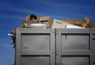 A dumpster filled with cardboard boxes against a blue sky.