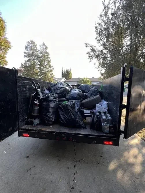 A dumpster filled with trash is parked in a driveway.