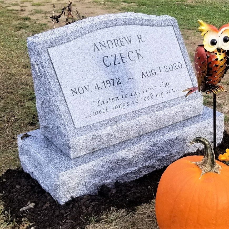 a gravestone for andrew r. czech is sitting next to a pumpkin in a cemetery .