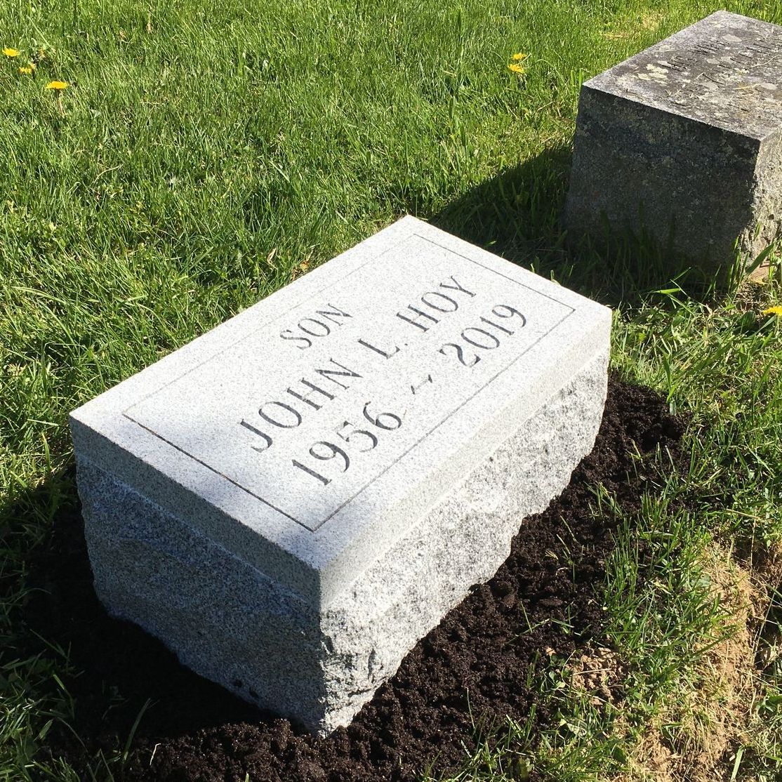 a gravestone for john l hoy is sitting in the grass in a cemetery .