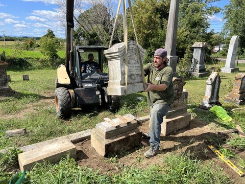 a man is lifting a gravestone in a cemetery with a forklift .
