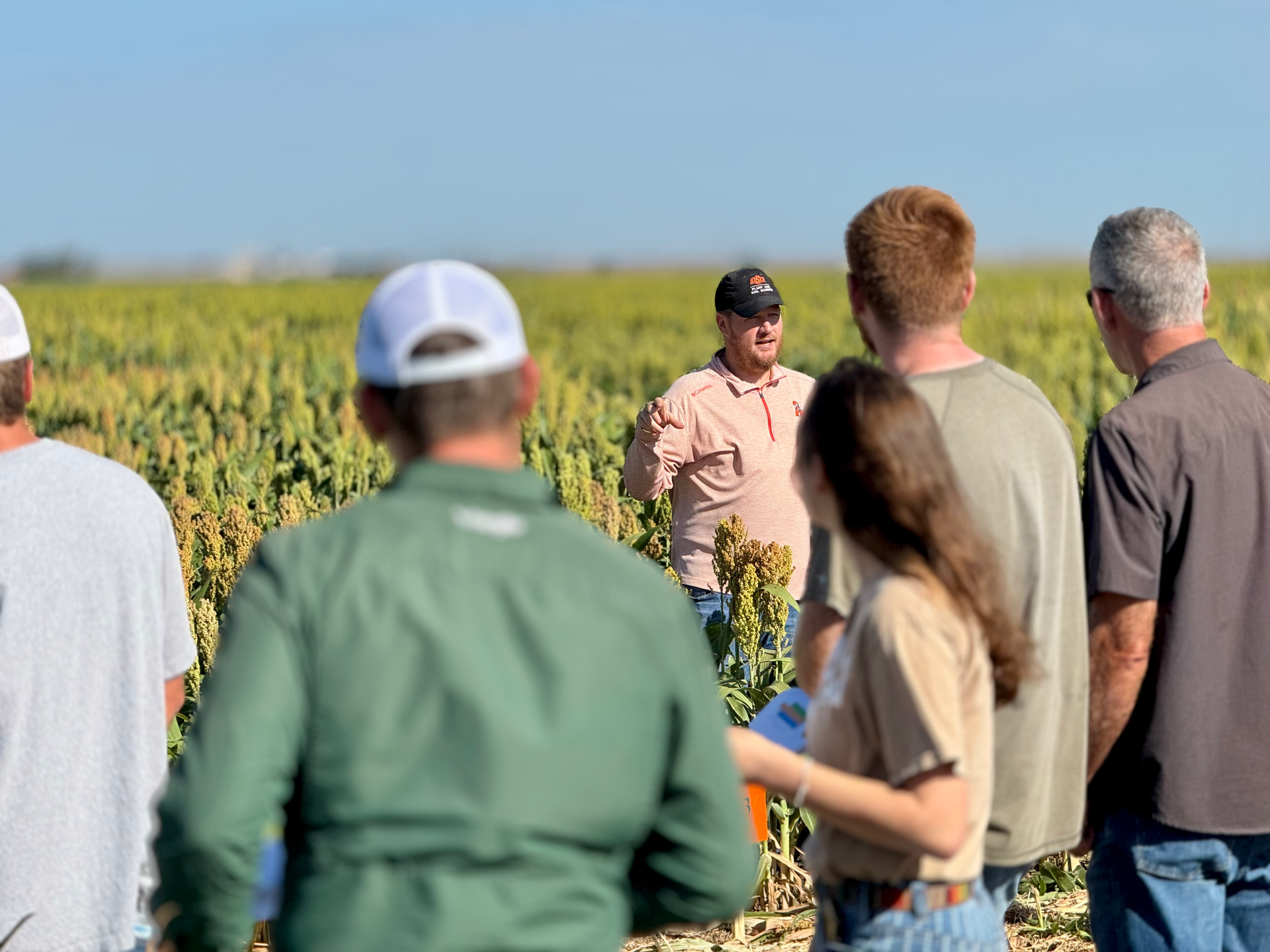 A group of people standing in a field with a man talking to them