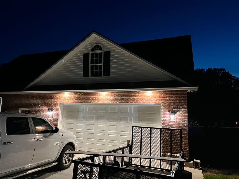 A white pickup truck parked in front of a brick garage with exterior lighting at dusk.