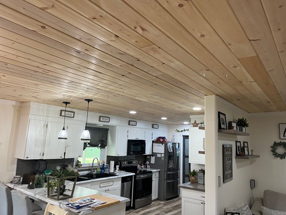 A kitchen with white cabinets, wood plank ceiling, two pendant lights, and dark stainless steel appliances.