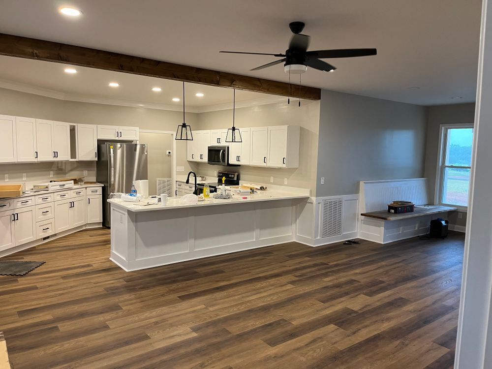 A bright, modern kitchen with white cabinets, a large island, wooden flooring, a ceiling fan, and a built-in bench seat.