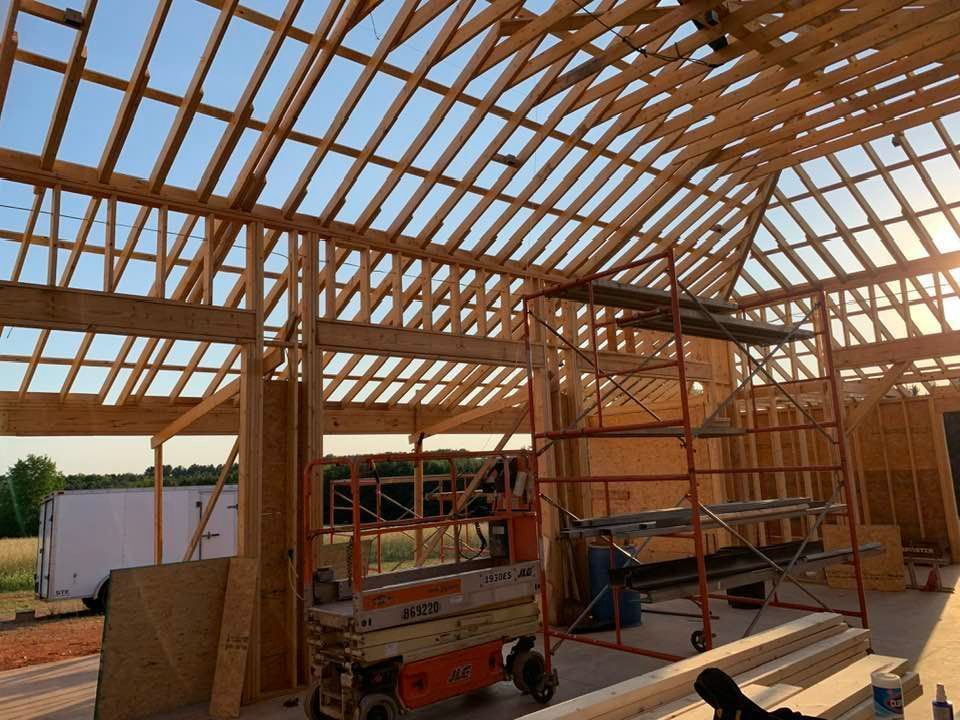 The wooden frame and rafters of a building under construction, with scaffolding and a scissor lift on the concrete floor.