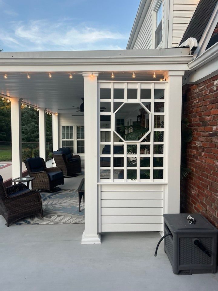 A white porch with a decorative lattice privacy screen, outdoor furniture, and string lights on a brick home patio.