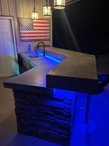 L-shaped stone bar with a concrete countertop, glowing blue LED lighting, and an American flag wall hanging.