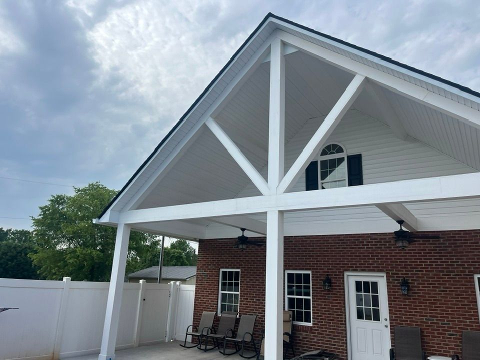 A large white triangular patio cover attached to a brick house with a paved patio and outdoor seating.