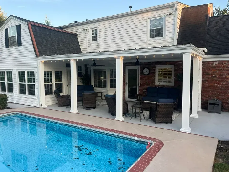 A backyard pool patio featuring a covered seating area with wicker furniture attached to a two-story residential home.