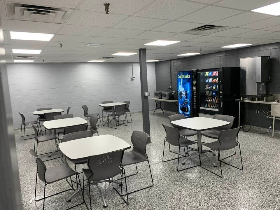 An empty breakroom with tables and chairs, a snack vending machine, a soda fountain, and a beverage dispenser.