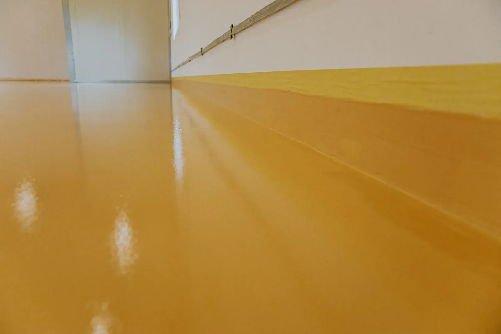 A shiny, yellow epoxy floor that curves upward to form a smooth, seamless baseboard against a white wall.