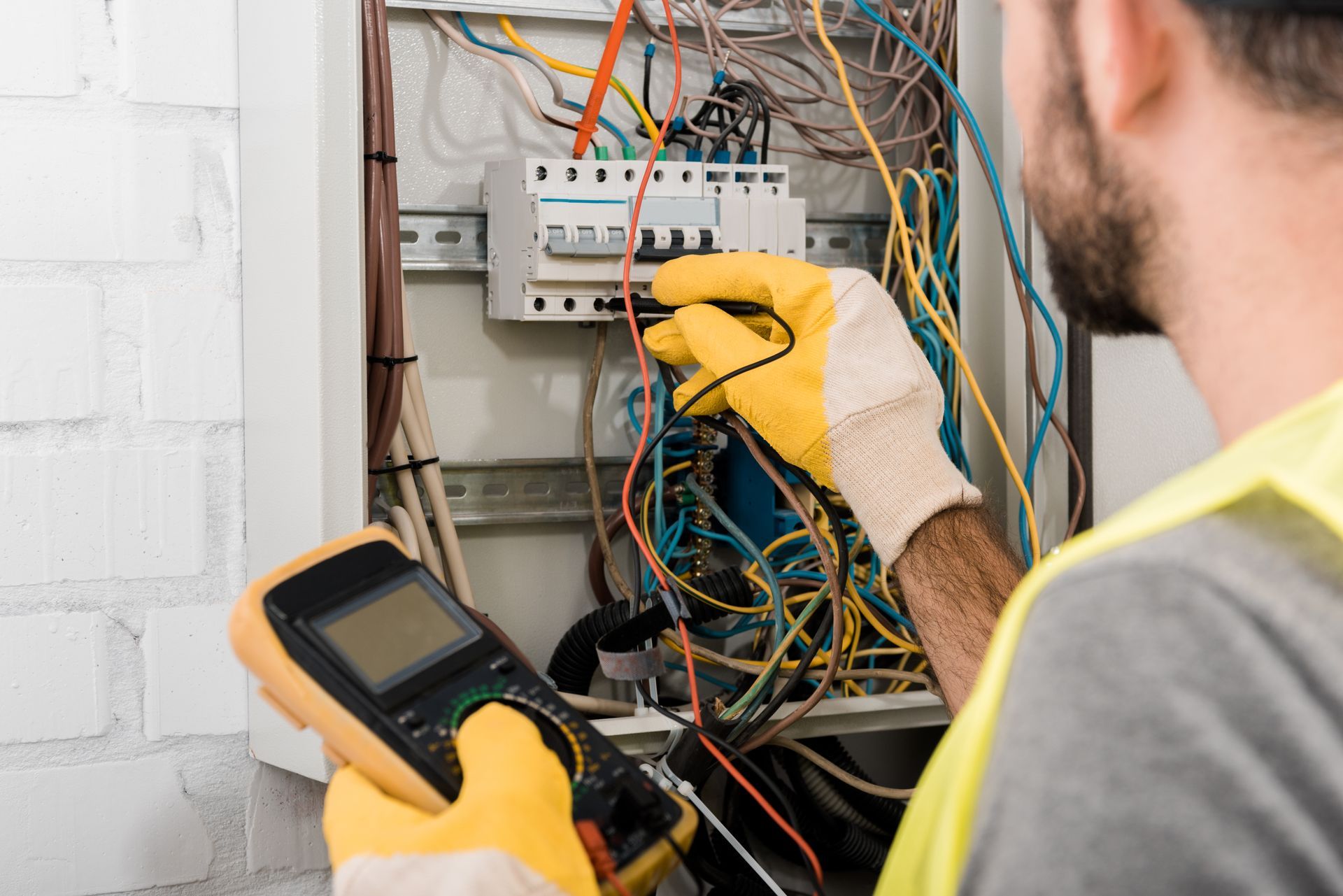 An electrician is working on an electrical box while holding a multimeter.