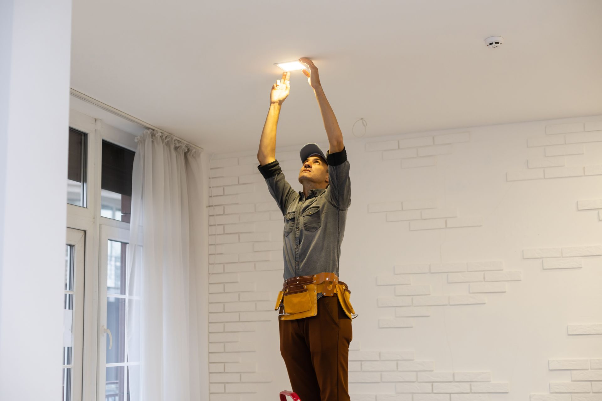 A man is hanging a light from the ceiling in a room.