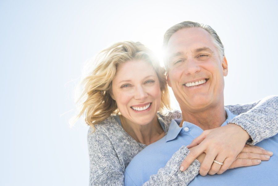 Smiling couple, woman embracing man from behind, bright sunlight.