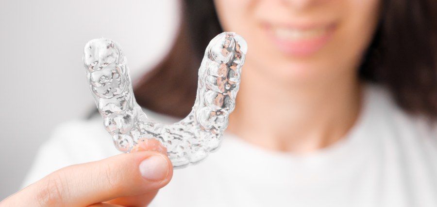 Person holding a clear dental retainer; smiling slightly.