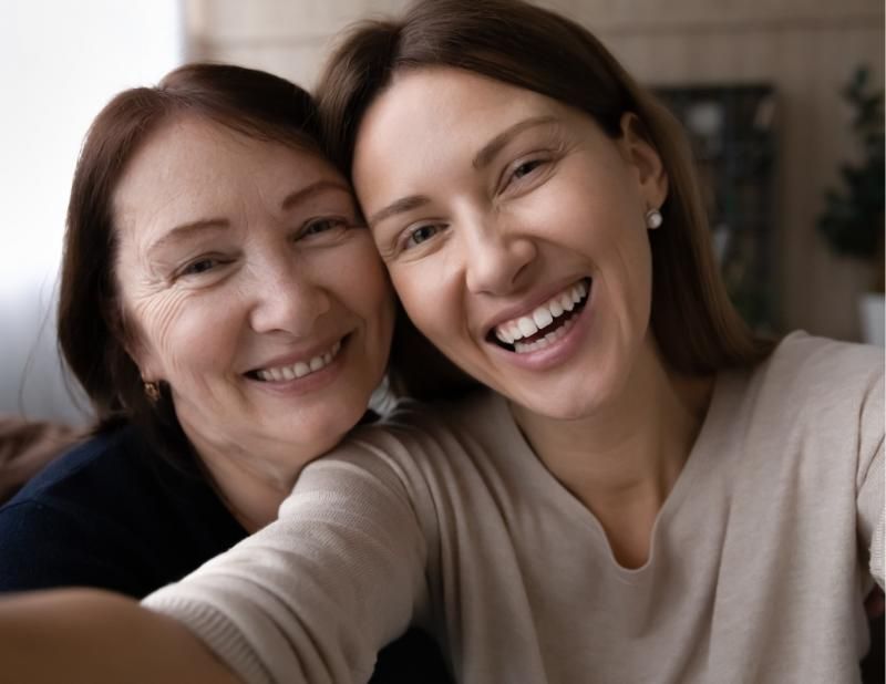 Two women smiling, taking a selfie. Indoors, blurred background.