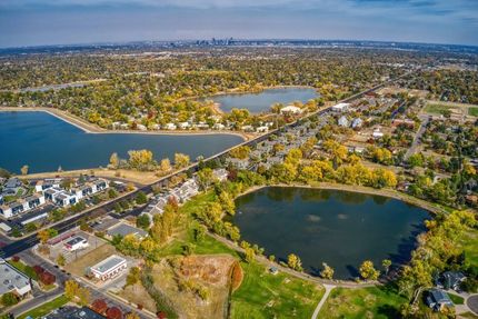 Aerial view of lakes, trees, houses, and the Denver skyline under a blue sky.