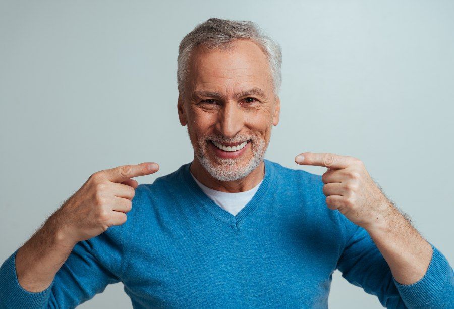 Man in blue sweater smiles, pointing to his teeth.