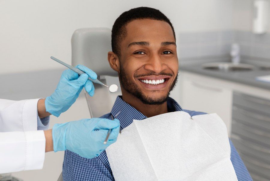 Man smiling in dental chair during checkup. Dentist hands with tools visible.
