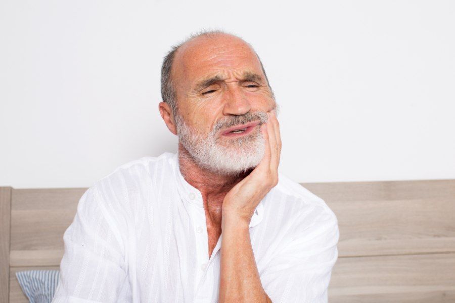 Man with beard grimaces, holding his jaw, showing signs of toothache pain.