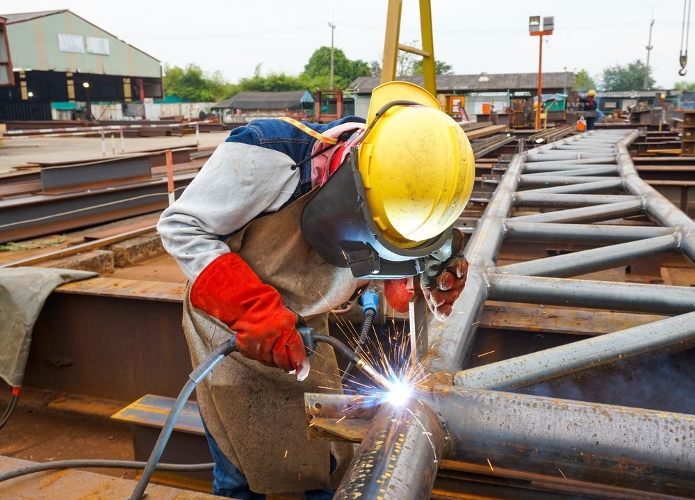 Welder in Yellow Hard Hat and Protective Gear Welding Metal Frame Outdoors — Chris Horton Manufacturing in Bathurst, NSW