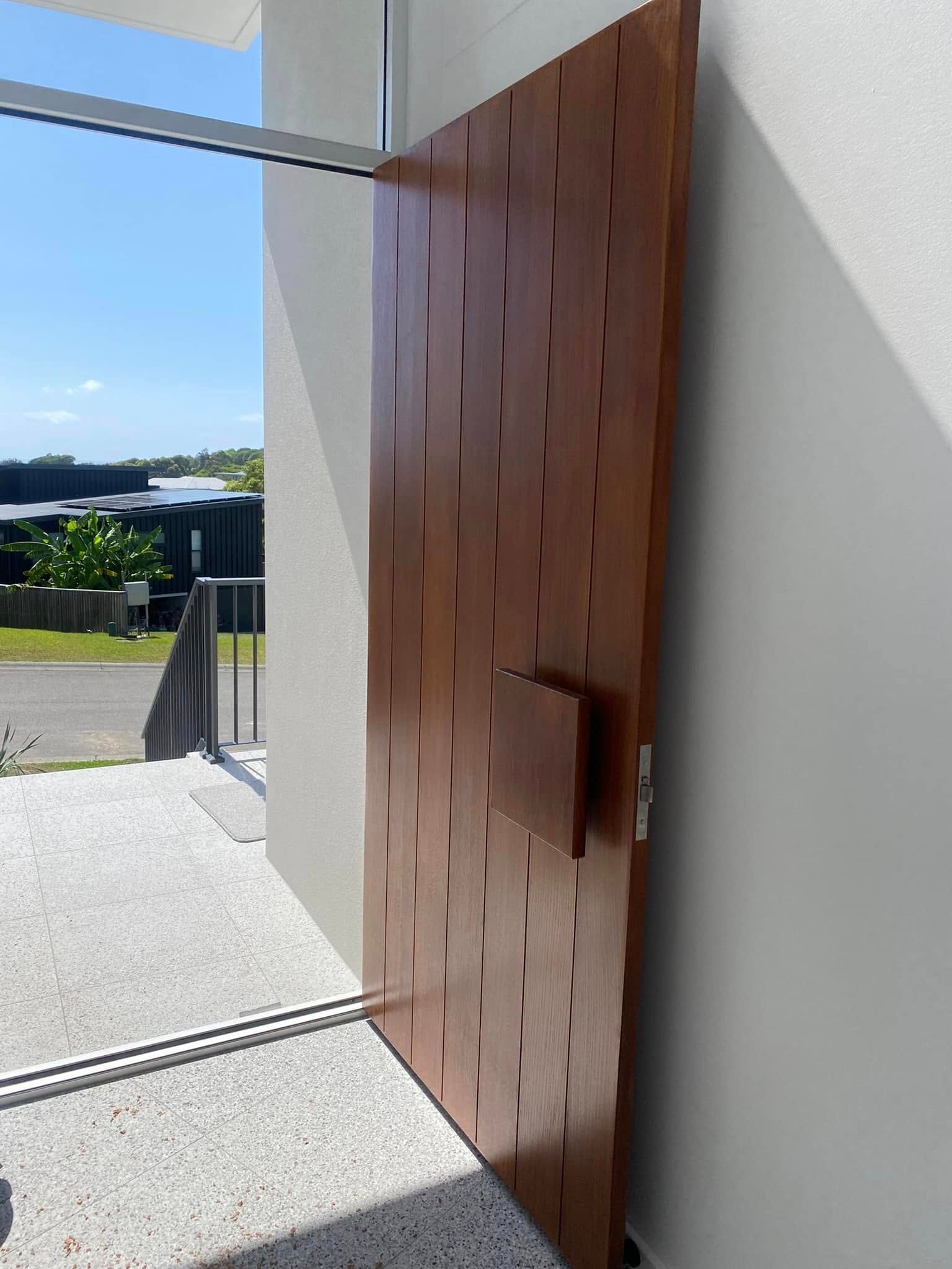 Open wooden door with rectangular cutouts, next to white wall. Steps and railing visible outside. — Barrington Coast Homes in Tallwoods, NSW