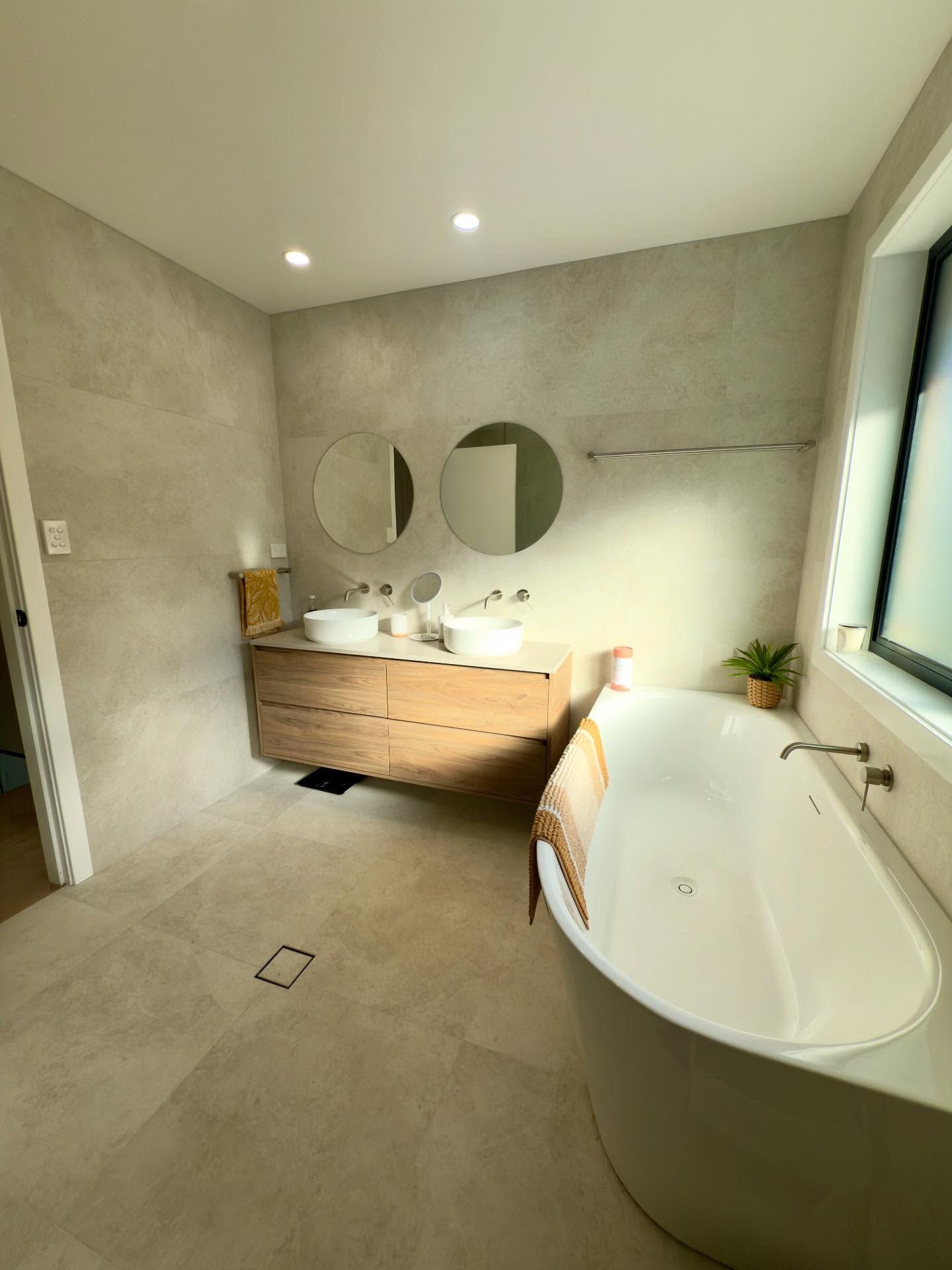 Modern Bathroom With a White Tub, Wood Vanity With Two Sinks, and Round Mirrors — Barrington Coast Homes in Forster, NSW
